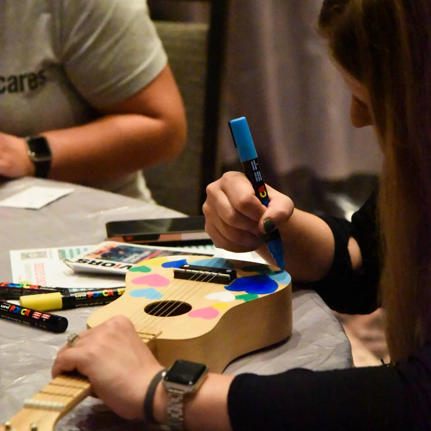 A guest decorates a small ukulele using colorful markers during a hands-on creative activity.