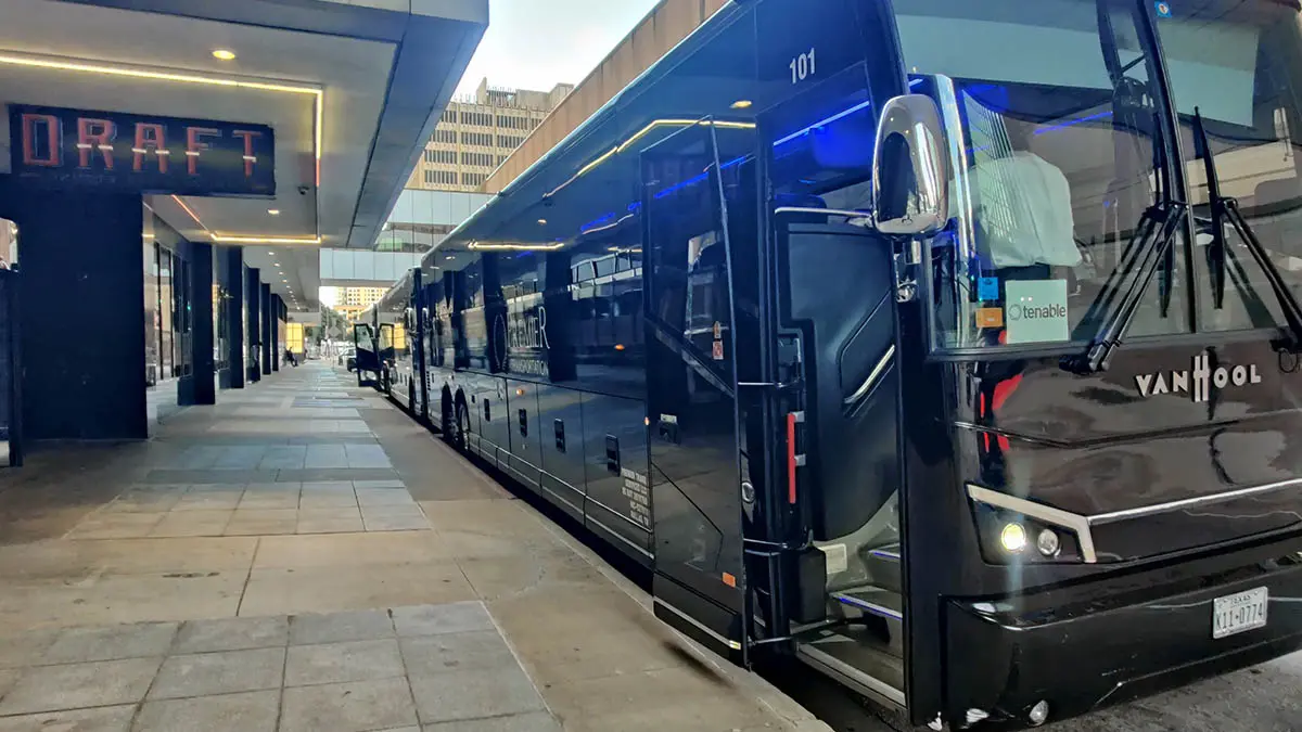 A Giant Tour bus parked on the street with doors open at the front of a hotel.